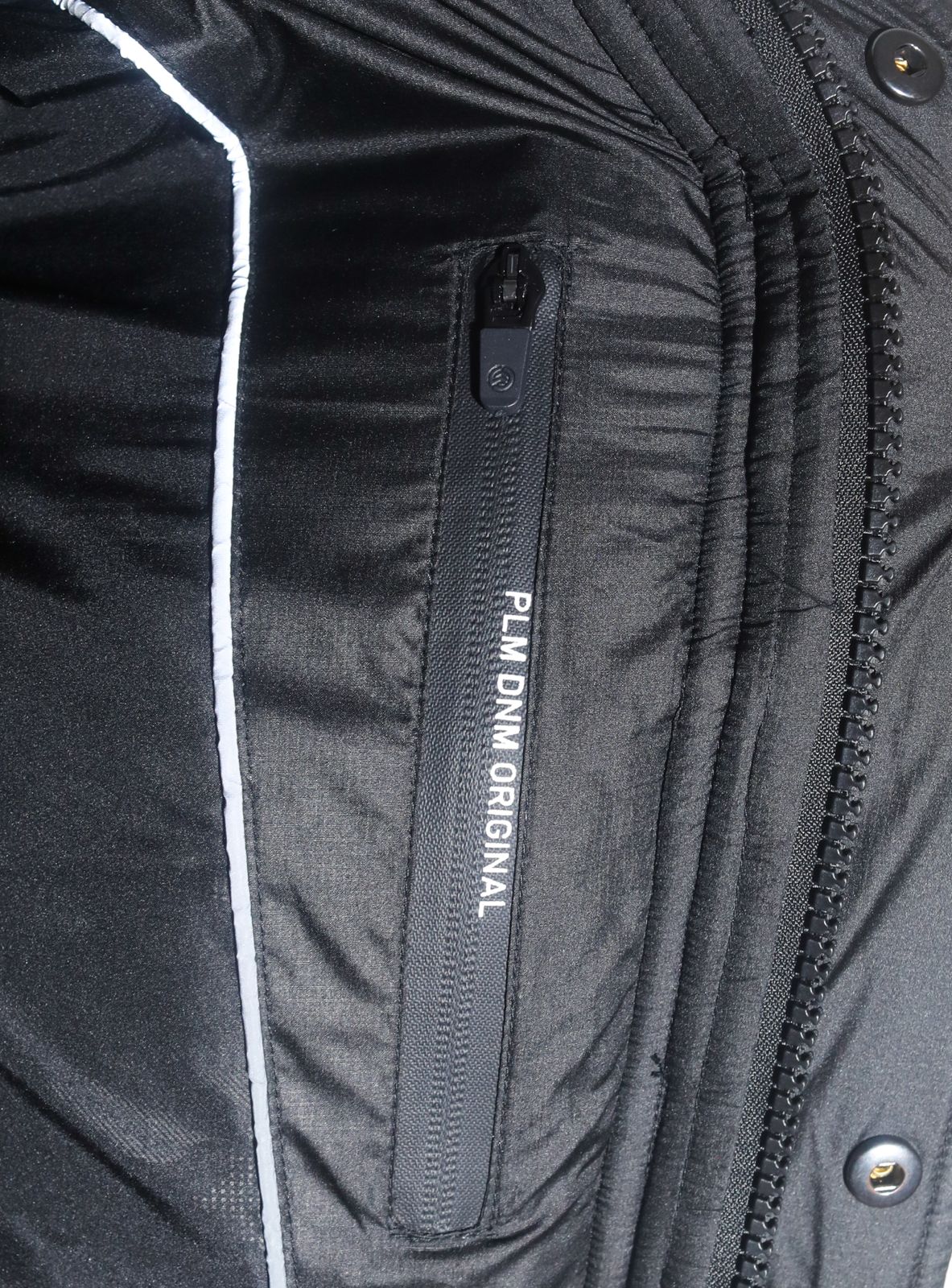 Nahaufnahme einer schwarzen Jacke mit Reißverschlusstasche und reflektierendem Paspel