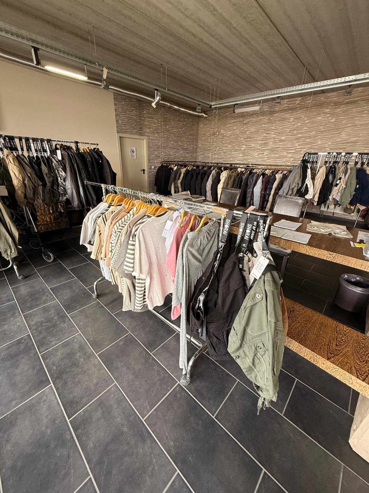 Kleiderständer mit Jacken, Westen und Shirts in einem Raum mit Holztisch